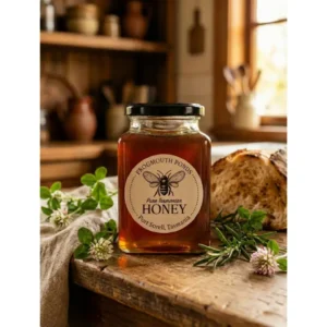 Jar of Frogmouth Ponds Pure Tasmanian Clover Honey with fresh clover blossoms on a rustic wooden table
